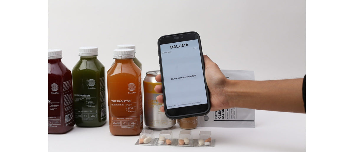 Hand hält Smartphone mit DALUMA Health Coach vor Saftflaschen