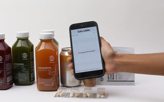 Smartphone mit dem DALUMA Health Coach Chat vor kaltgepressten Säften, Kombucha und Detox Clearing Mask.