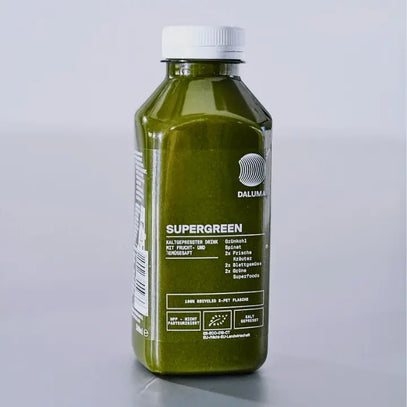 Eine durchsichtige Plastikflasche, gefüllt mit grünem Saft mit der Aufschrift SUPERGREEN, steht auf einer hellgrauen Fläche. Auf dem Etikett sind Inhaltsstoffe und Nährwertangaben aufgeführt. Die Flasche hat einen weißen Verschluss und ein modernes, einfaches Design.