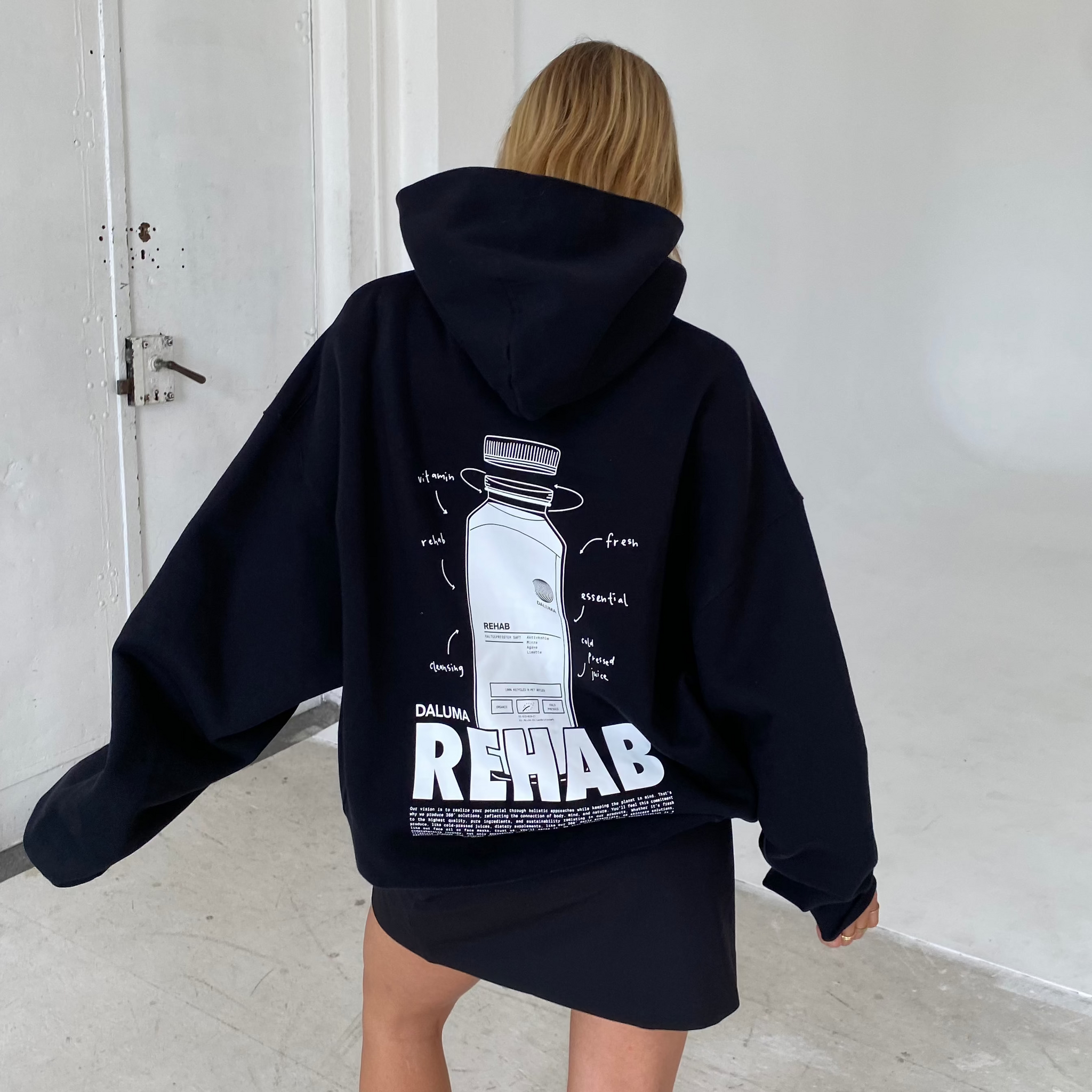 Eine Person mit langen blonden Haaren trägt den DALUMA JOSEPH ATELIER X DALUMA REHAB HOODIE mit grafischem Muster und dem Schriftzug 