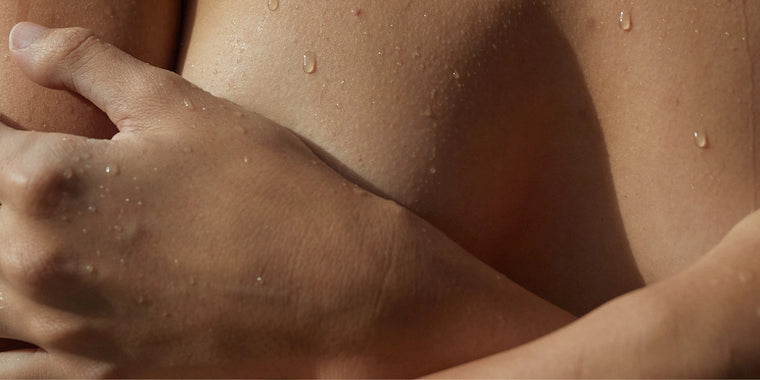 Eine Nahaufnahme des Arms und der Schulter einer Person mit Wassertropfen auf der Haut, die darauf hindeuten, dass sie nass ist oder gerade aus dem Wasser kommt. Der Arm ist über der Brust gekreuzt.