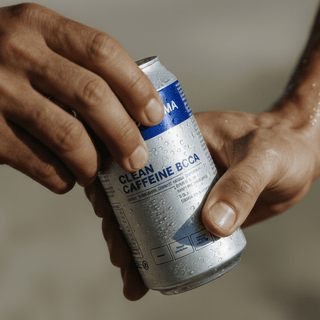 Eine Person hält eine kalte, silberne Dose mit DALUMA CLEAN BCAA ENERGY DRINK, auf deren Oberfläche Tautropfen glitzern. Das Etikett hebt sich ab, während die Hände sich darauf vorbereiten, die Dose zu öffnen, während der unscharfe Hintergrund den Fokus auf das Produkt lenkt.