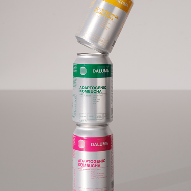 Drei Dosen DALUMA GLOW UP GREENS MARACUJA KOMBUCHA sind vor einem schlichten, hellen Hintergrund gestapelt und strotzen nur so vor probiotischen Kulturen zur Unterstützung deiner Darmgesundheit.