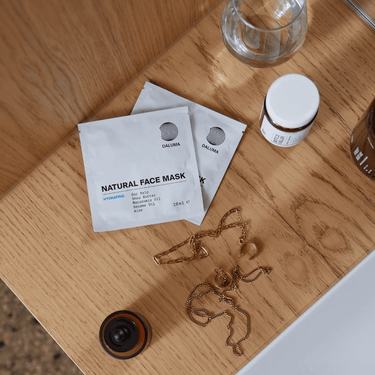 Drei DALUMA 3x MASK DUO-Pakete, ein kleiner Krug, ein Glasbecher und Goldschmuck sind auf einer Holzfläche neben einem weißen Waschbecken ausgestellt.