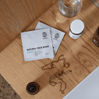 Drei DALUMA 3x MASK DUO-Pakete, ein kleiner Krug, ein Glasbecher und Goldschmuck sind auf einer Holzfläche neben einem weißen Waschbecken ausgestellt.