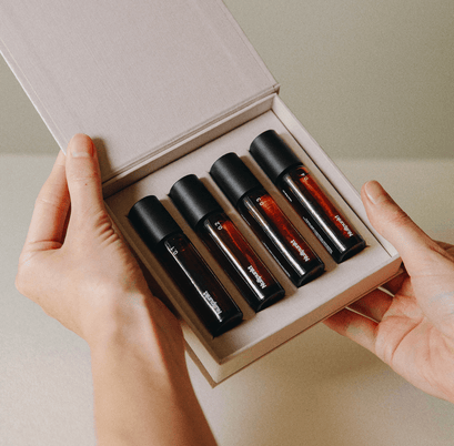 Eine Person hält eine geöffnete Schachtel in der Hand, die vier dunkle Glasflaschen mit schwarzen Verschlüssen enthält, die fein säuberlich in einer cremefarbenen Schaumstoffeinlage angeordnet sind - das ist die NULLPUNKT COMPLETE COLLECTION von Nullpunkt.