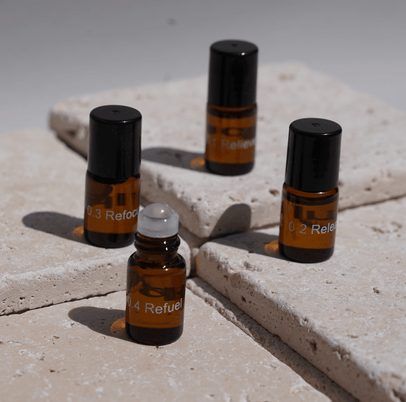 Vier kleine braune Glasflaschen mit schwarzen Verschlüssen, beschriftet mit 